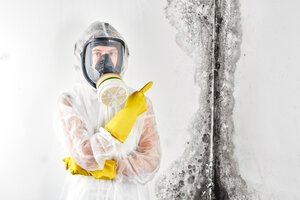 Mold mitigation expert dressed in protective clothing pointing out the presence of black mold